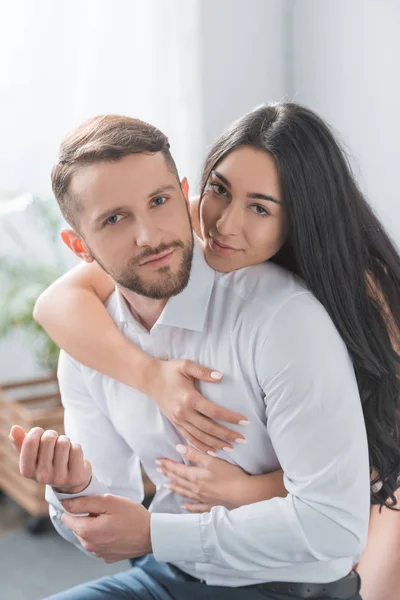 Novia feliz abrazando novio barbudo en camisa blanca en casa - foto de stock