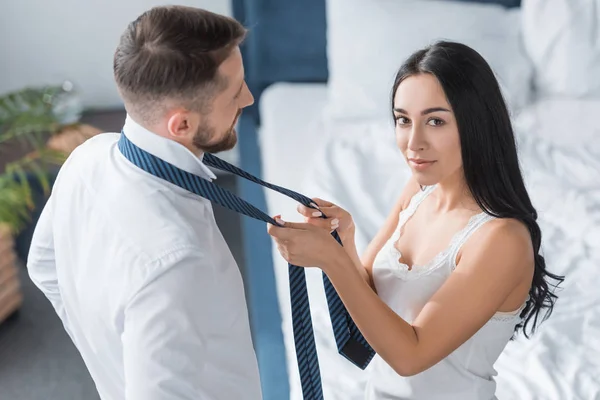 Вид зверху красива жінка зв'язує краватку бородатого чоловіка в спальні — стокове фото