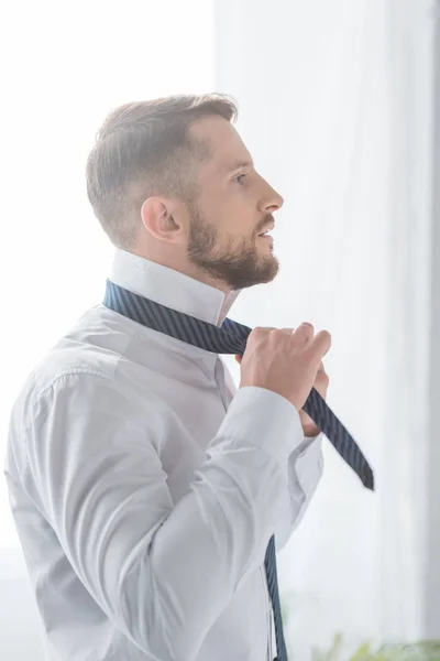 Handsome bearded man in white shirt touching tie — Stock Photo