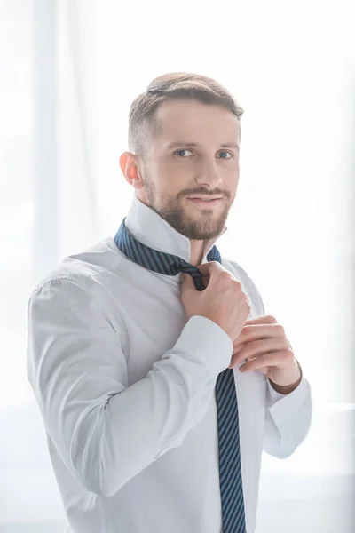 Felice uomo barbuto in abito formale sorridente mentre si tocca cravatta — Foto stock