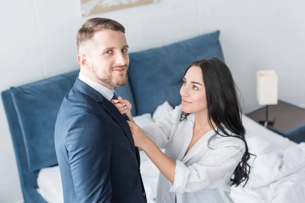Overhead view of cheerful brunette woman touching tie of happy man standing at home — Stock Photo