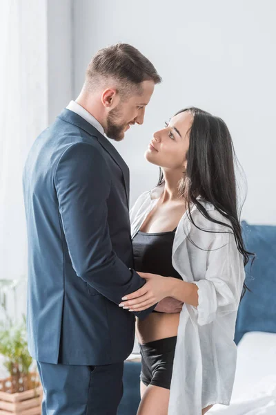 Happy bearded man in suit hugging attractive girlfriend in white shirt — Stock Photo