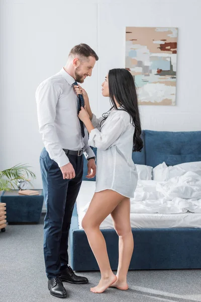 Attraente fidanzata in bianco camicia toccare cravatta di bello fidanzato in vestito — Foto stock