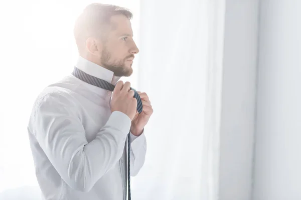 Successful man in white shirt touching tie while standing at home — Stock Photo