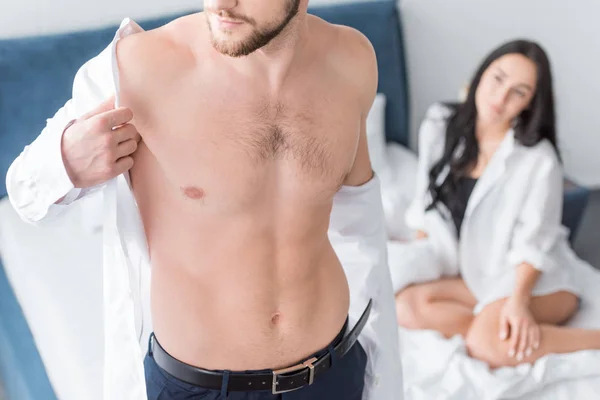 Vista recortada de hombre musculoso con camisa blanca cerca de la mujer en la cama - foto de stock