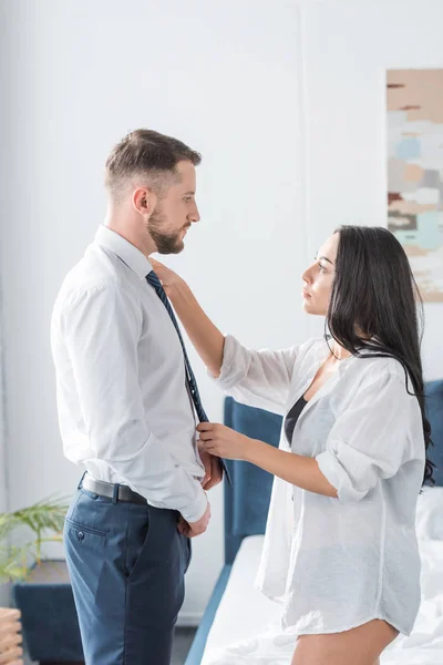 Attraktive Frau berührt Hemd eines gutaussehenden bärtigen Mannes, der in formeller Kleidung steht — Stockfoto