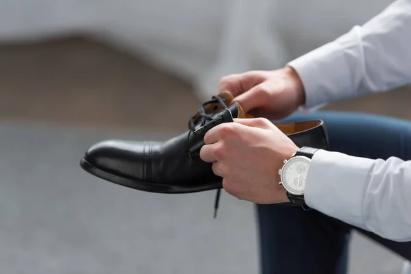Vista recortada del hombre con reloj en la mano que sostiene zapato negro - foto de stock