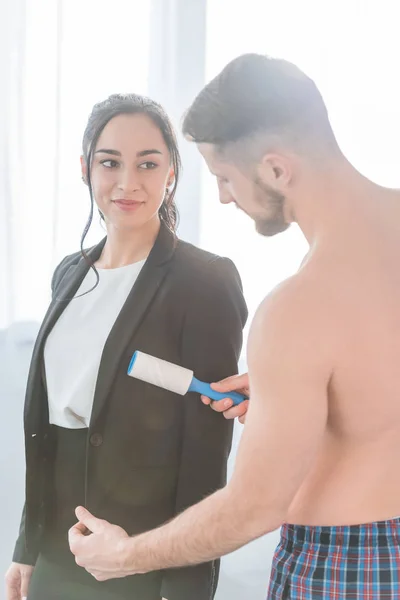 Bearded muscular man cleaning formal wear of happy brunette woman — Stock Photo