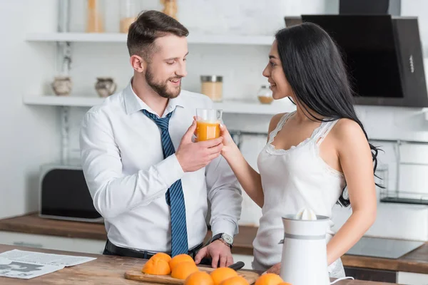 Donna bruna allegra che tiene il bicchiere di gustoso succo d'arancia vicino all'uomo in giacca e cravatta — Foto stock