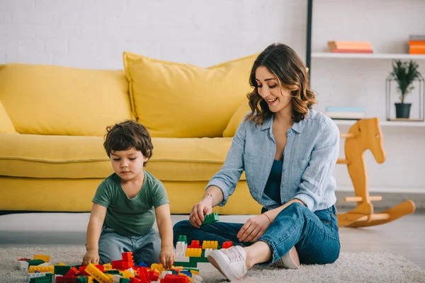 Mamá e hijo jugando con bloques de juguete en la sala de estar - foto de stock