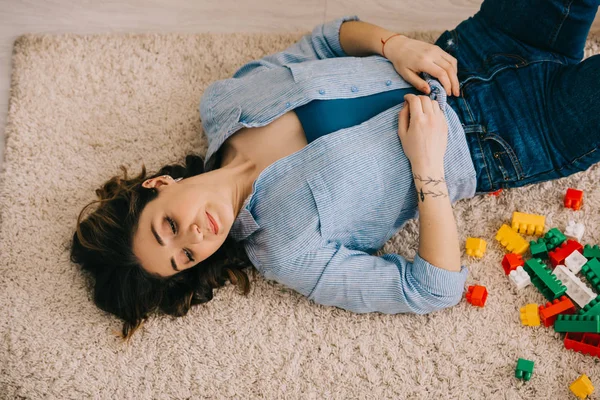 Ansicht einer müden Frau, die mit bunten Spielzeugklötzen auf Teppich liegt — Stockfoto