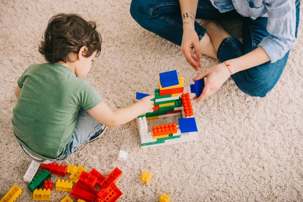 Обрізаний вид на маму і сина, що грає з іграшковими блоками на килимі — стокове фото