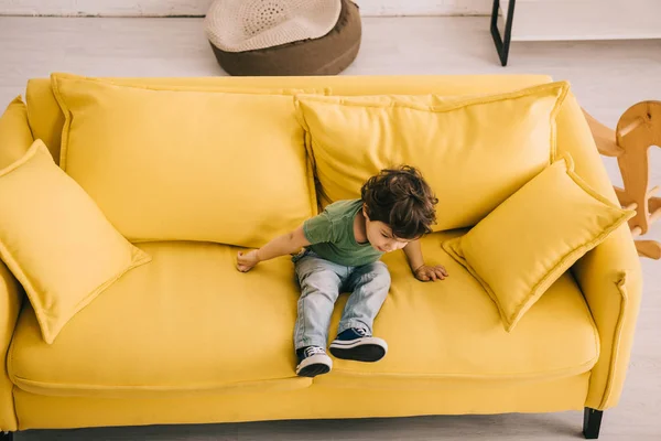 Petit garçon en t-shirt vert assis sur canapé jaune — Photo de stock