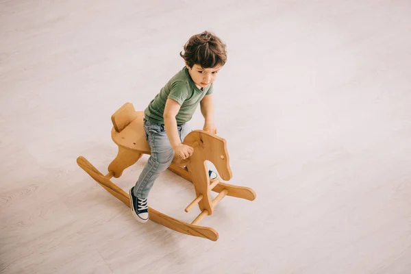 Vue aérienne du petit garçon en t-shirt vert chevauchant un cheval à bascule — Photo de stock