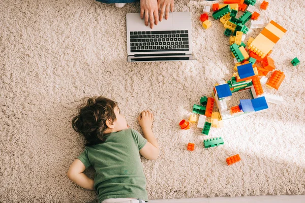 Cropped view of mother using laptop and son lying on carpet — Stock Photo