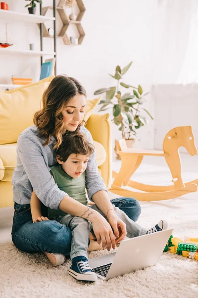 Mom and son sitting on carpet and using laptop — Stock Photo