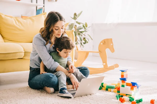 Mom and son sitting on carpet and using laptop — Stock Photo