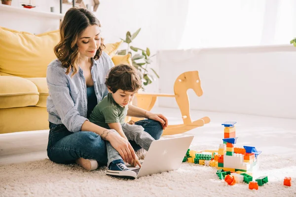 Mom and son sitting on carpet and using laptop — Stock Photo