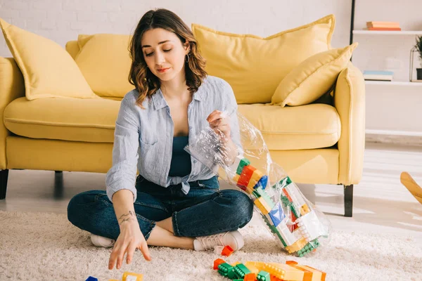 Müde Frau in Jeans sitzt auf Teppich mit Spielzeugklötzen — Stockfoto