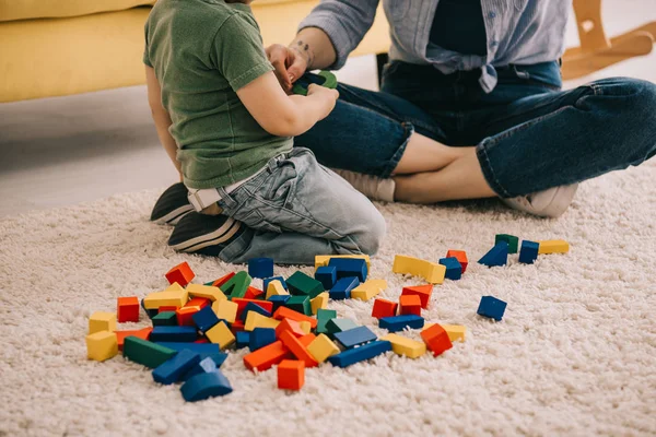 Обрезанный вид матери и сына, играющих с игрушечными блоками на ковре — стоковое фото