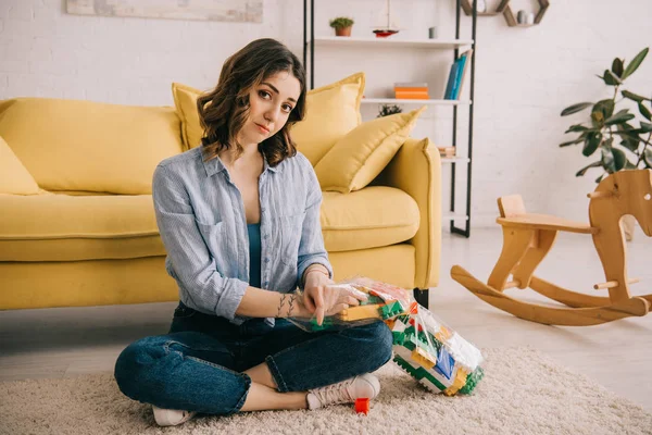 Femme fatiguée avec des blocs de jouets assis sur le tapis avec les jambes croisées — Photo de stock