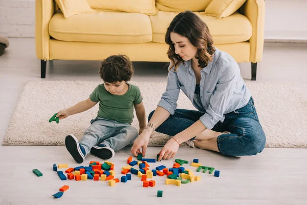 Мать и сын играют с игрушечными блоками на ковре — стоковое фото