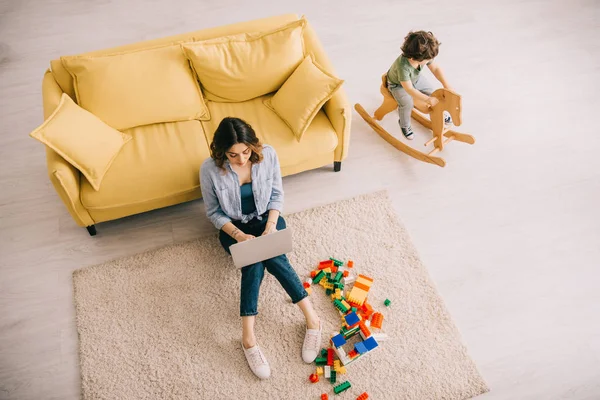 Overhead view of mother using laptop while son sitting on rocking horse — Stock Photo