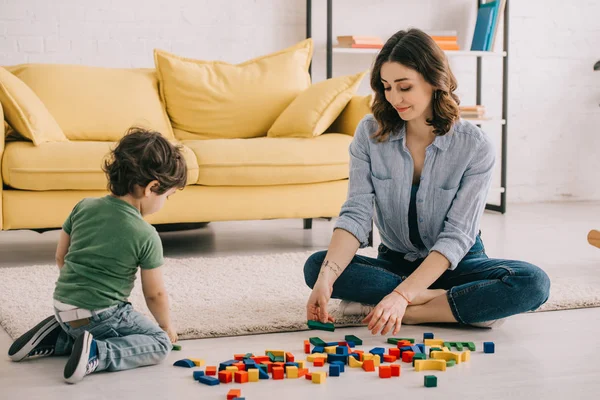 Мать и сын играют с игрушечными блоками на ковре — стоковое фото