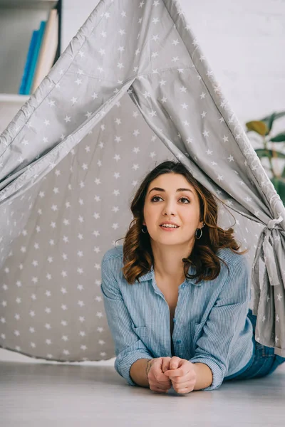 Mujer joven inspirada acostada en wigwam gris en casa - foto de stock