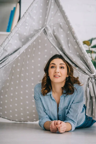 Inspired young woman lying in grey wigwam at home — Stock Photo