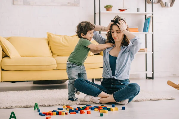 Madre stanca che tocca la testa mentre gioca con il figlio — Foto stock