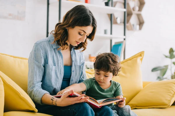 Maman et son fils assis sur le canapé jaune et le livre de lecture — Photo de stock