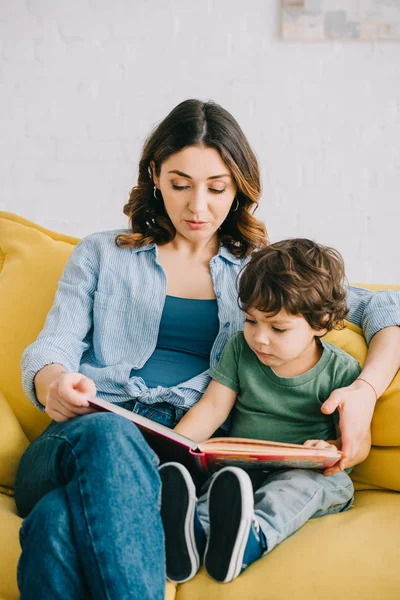 Maman et son fils assis sur le canapé jaune et le livre de lecture — Photo de stock