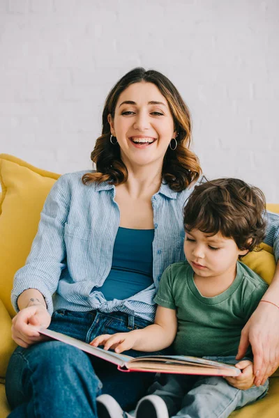 Mãe e filho sentados no sofá amarelo e livro de leitura — Fotografia de Stock