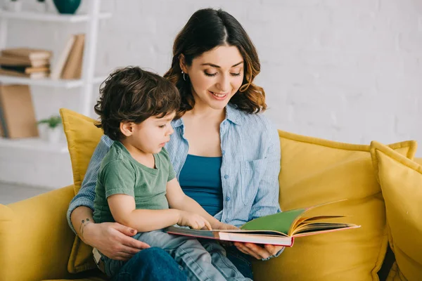 Mom and son sitting on yellow sofa and reading book — Stock Photo
