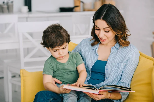 Maman et son fils assis sur le canapé jaune et le livre de lecture — Photo de stock