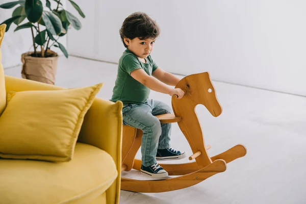 Bonito menino sentado no cavalo de balanço de madeira na sala de estar — Fotografia de Stock