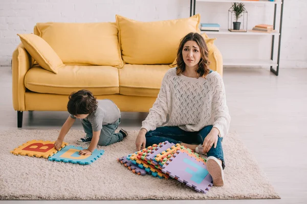Traurige Mutter und Sohn spielen mit Alphabet-Puzzlematte auf Teppich — Stockfoto