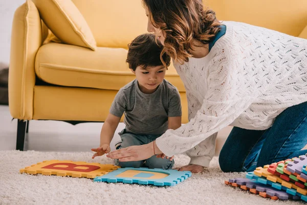 Madre e hijo jugando con alfabeto alfombra rompecabezas en la alfombra - foto de stock