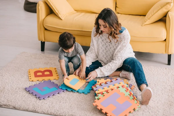 Mother and son playing with alphabet puzzle mat on carpet — Stock Photo