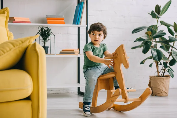 Cute child sitting on wooden rocking horse in living room — Stock Photo