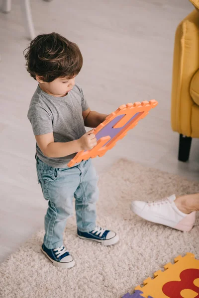 Vue grand angle de l'enfant étudiant les lettres tout en jouant avec le tapis de puzzle — Photo de stock