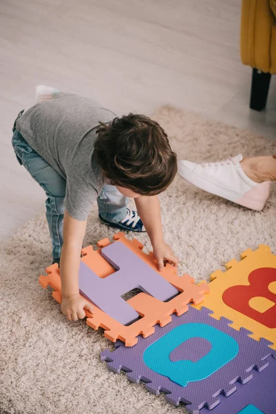 Bambino che gioca con tappetino puzzle alfabeto su tappeto — Foto stock