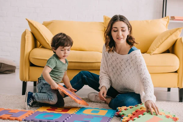 Mother and son playing with alphabet puzzle mat on carpet — Stock Photo