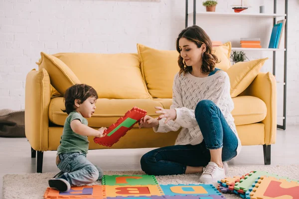 Mãe e filho brincando com tapete de quebra-cabeça alfabeto no tapete — Fotografia de Stock