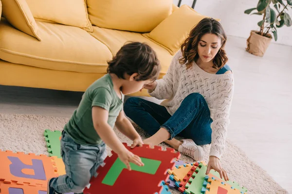 Mother and son playing with alphabet puzzle mat on carpet — Stock Photo