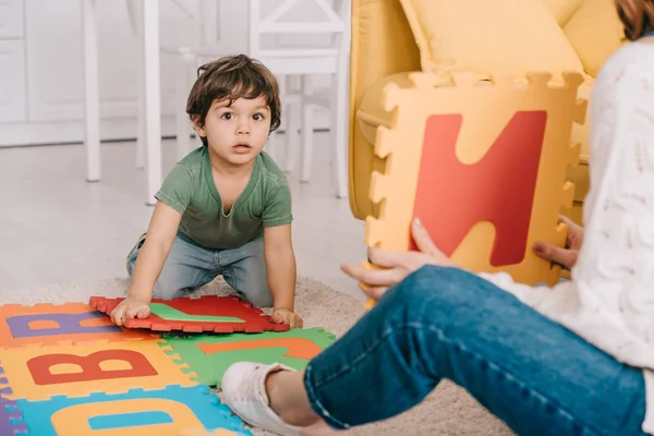 Cropped view of mother and son playing with alphabet puzzle mat — Stock Photo