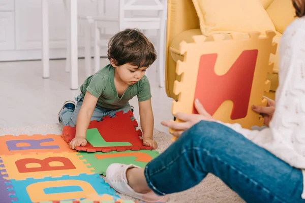 Vista recortada de la madre y el hijo jugando con el alfabeto alfombra del rompecabezas - foto de stock