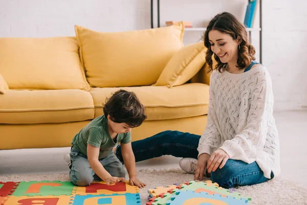 Sorrindo mãe e criança brincando com tapete de quebra-cabeça alfabeto — Fotografia de Stock