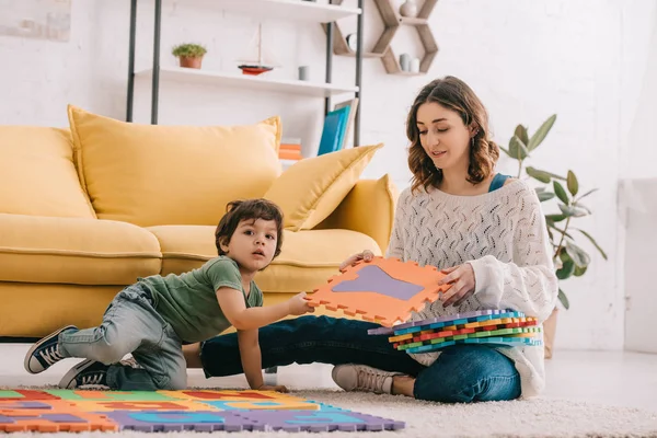 Sorridente madre e bambino che giocano con il tappetino puzzle alfabeto — Foto stock
